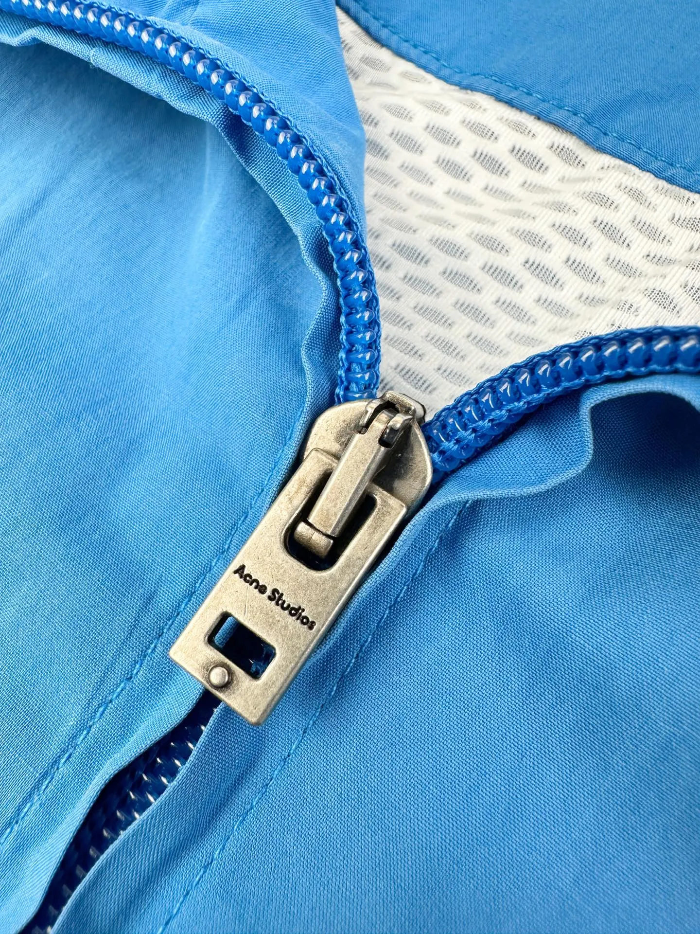 Acnee Studios contrasting logo zipper jacket, custom-made dusty royal poplin, lightweight and crisp, dry and wind-resistant, sophisticated Royal Blue halo body, washed mist to soften the bright tones, interpreting the cool and relaxed luxury unique to Scandinavia, stand-up collar fully zipped coach jacket, cuffs hem elastically gathered, creating a relaxed, drop-top short silhouette, fully lined inside, smooth and neat upper body The Acne Studios print is discreetly engraved on the chest, retaining the brand gene in a restrained and subtle manner. The contrasting Acne Studios Retro emblem is laid out on the back of the garment. One simple and one complex form a clever visual contrast, which reflects the brand's heritage and traces back to the origin of the brand. It uses the Nordic minimalist high-end ready-to-wear language to describe the narrative of relaxed and restrained luxury and elegance. Process 1: Adopt glue printing process. The printing has been revised three times with the film screen. Use glue liquid paint to print the pattern on the fabric. Bake the fabric to fix the printed pattern. Process 2: Gradient distressed spray process. By spraying dyes of different colors on the surface of the fabric, the clothes can show rich color changes under different lights and increase the visual layering. Process 3: Heavy fermentation washing uses a special solution to remove stains and slight fading, and then snowflake washing. Use strong washing to fade the color to make the color more uniform. Process 4: The hem is made in one go using a three-needle waist-drawing machine. The elastic band and the fabric are sewn together in the same process using the special needle position and feeding mechanism of the machine. The three-needle design is more secure and can distribute pressure evenly to ensure that the elastic band and the fabric are tightly fitted. Accessories: Customized 1:1 Acne zipper Customized 1:1 Acne trademark Version: Loose version Size: 42 44 46 48 Style number: 25254